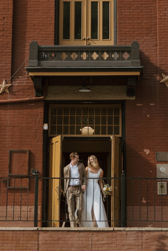 Happy couple walking out of the courthouse in downtown Durango, smiling and holding hands, celebrating their newlywed moment.