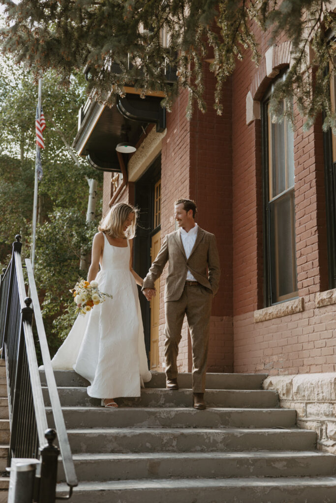 Couple joyfully walking down the courthouse steps in Telluride, hand in hand, with smiles on their faces as they celebrate their marriage.