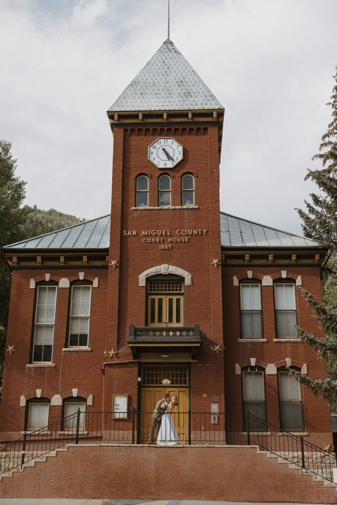 Couple standing outside the historic Telluride courthouse after their elopement, with smiles and mountain views in the background.